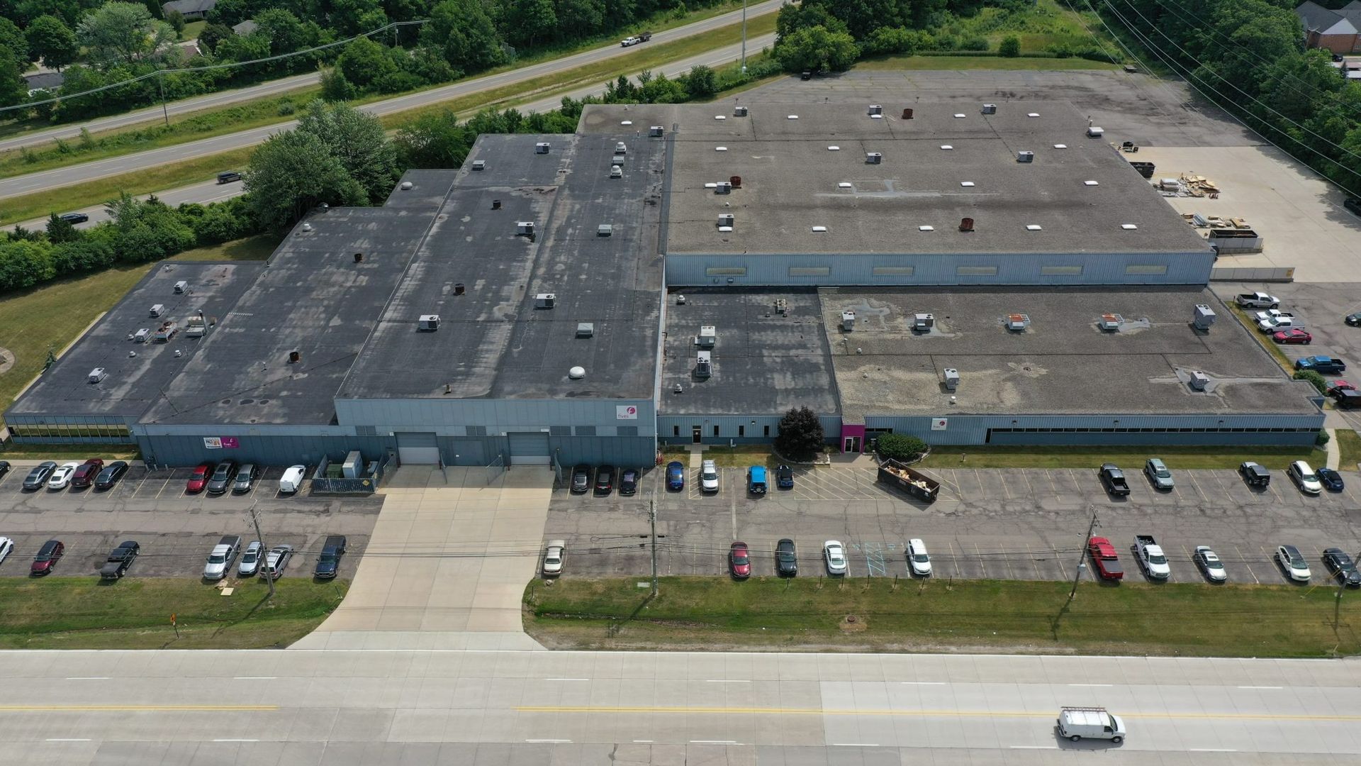 Aerial view of a large commercial building with parking lots, road frontage, and a few cars.