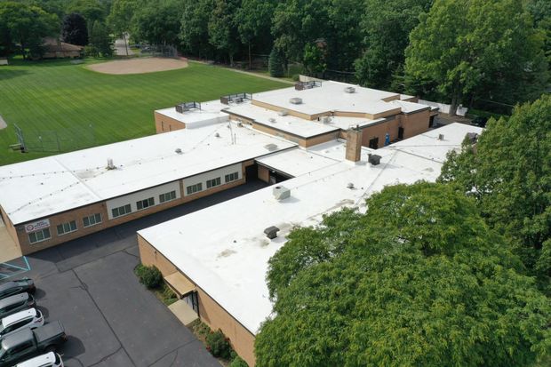 Aerial view of a white-roofed school building beside a green field and trees