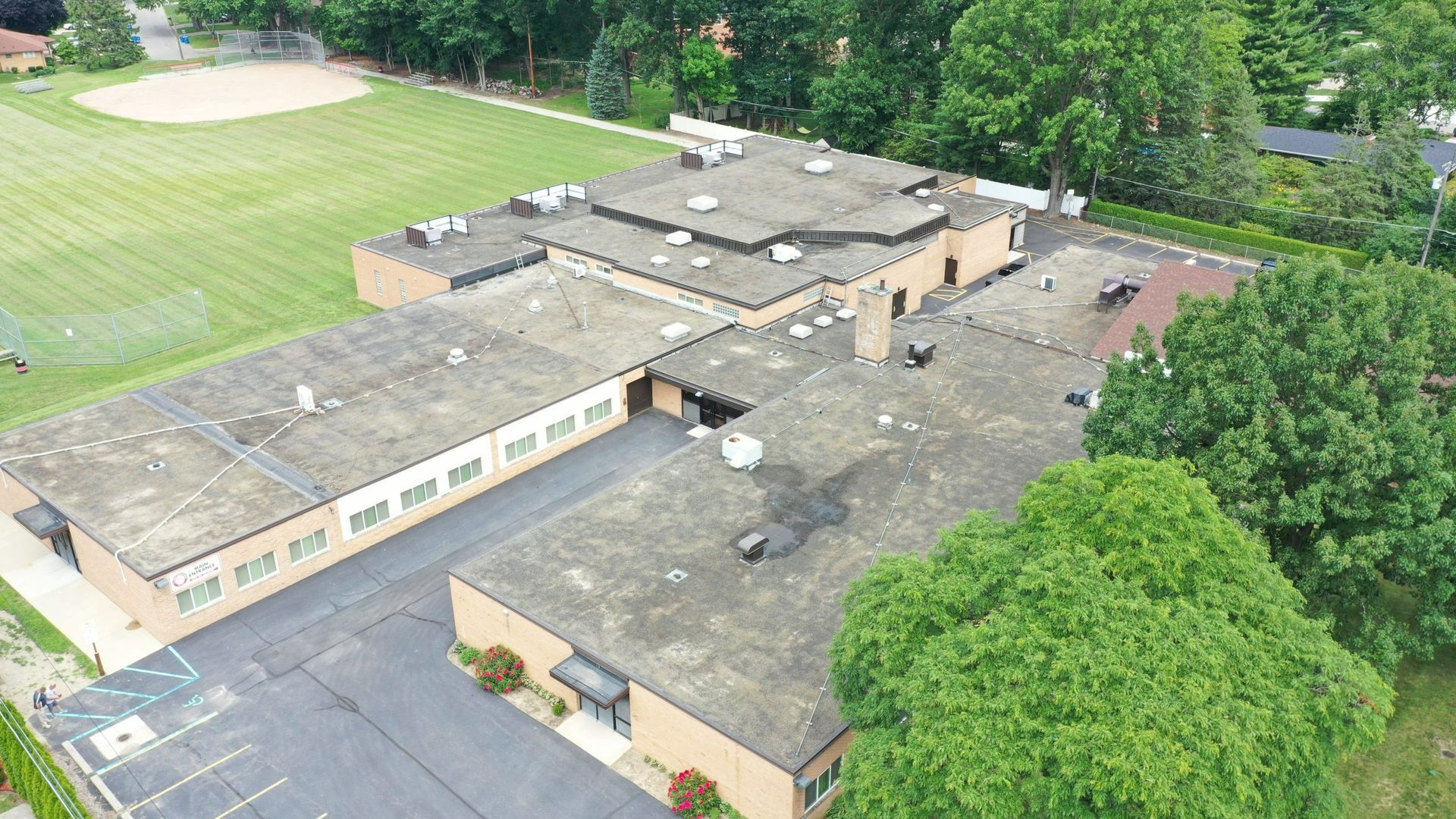 Aerial view of a flat-roof school building beside a sports field and trees