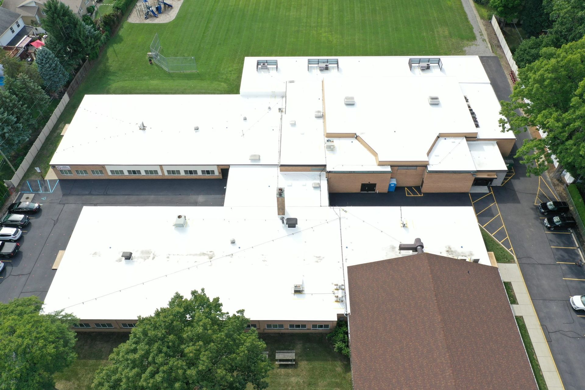 Aerial view of a large white-roofed building with surrounding grass and parked cars.