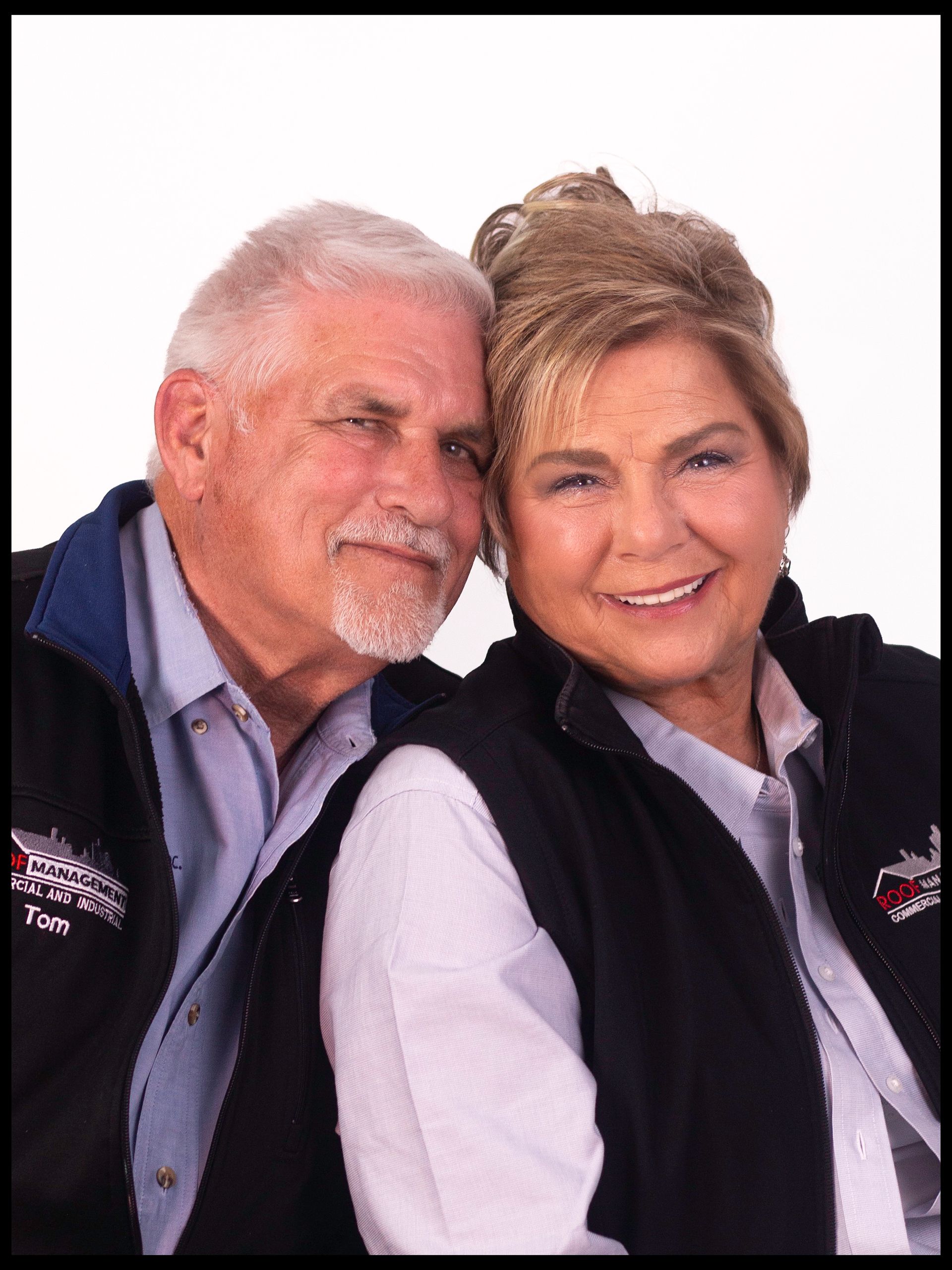 Smiling couple posing together, wearing navy vests against a white background
