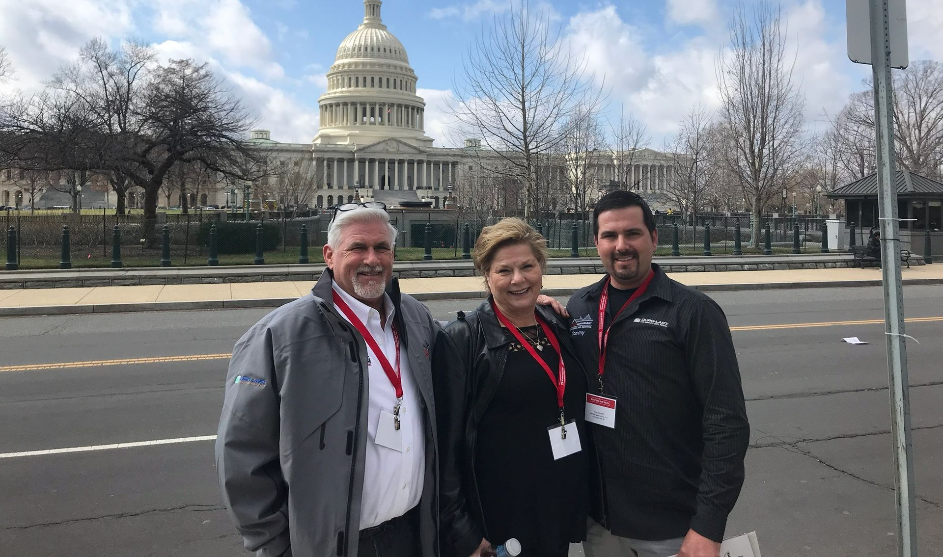 Three people posing in front of the U.S. Capitol building on a cloudy day.