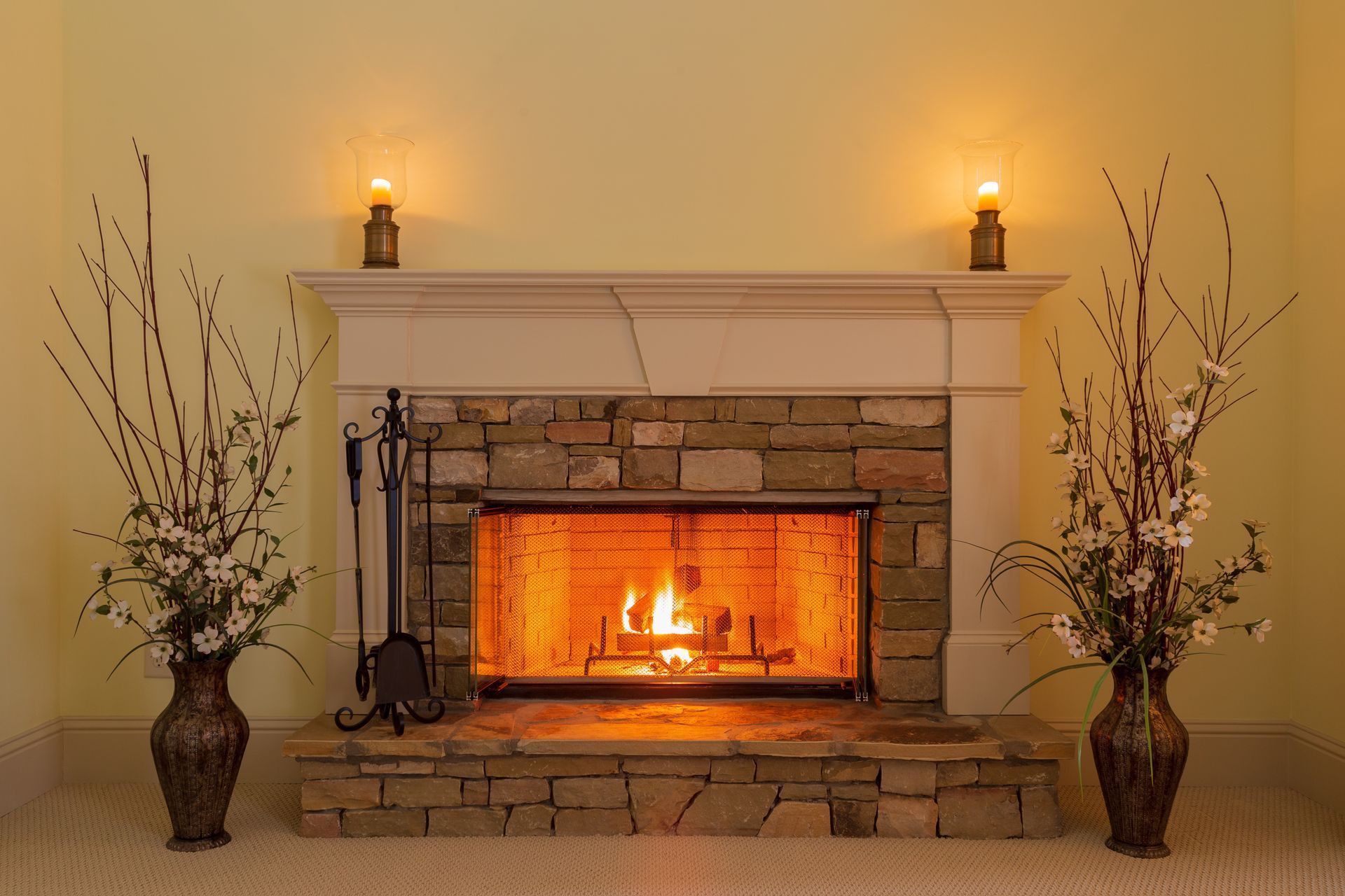 Cozy living room fireplace with burning fire, stone surround, candles, and tall vases on both sides