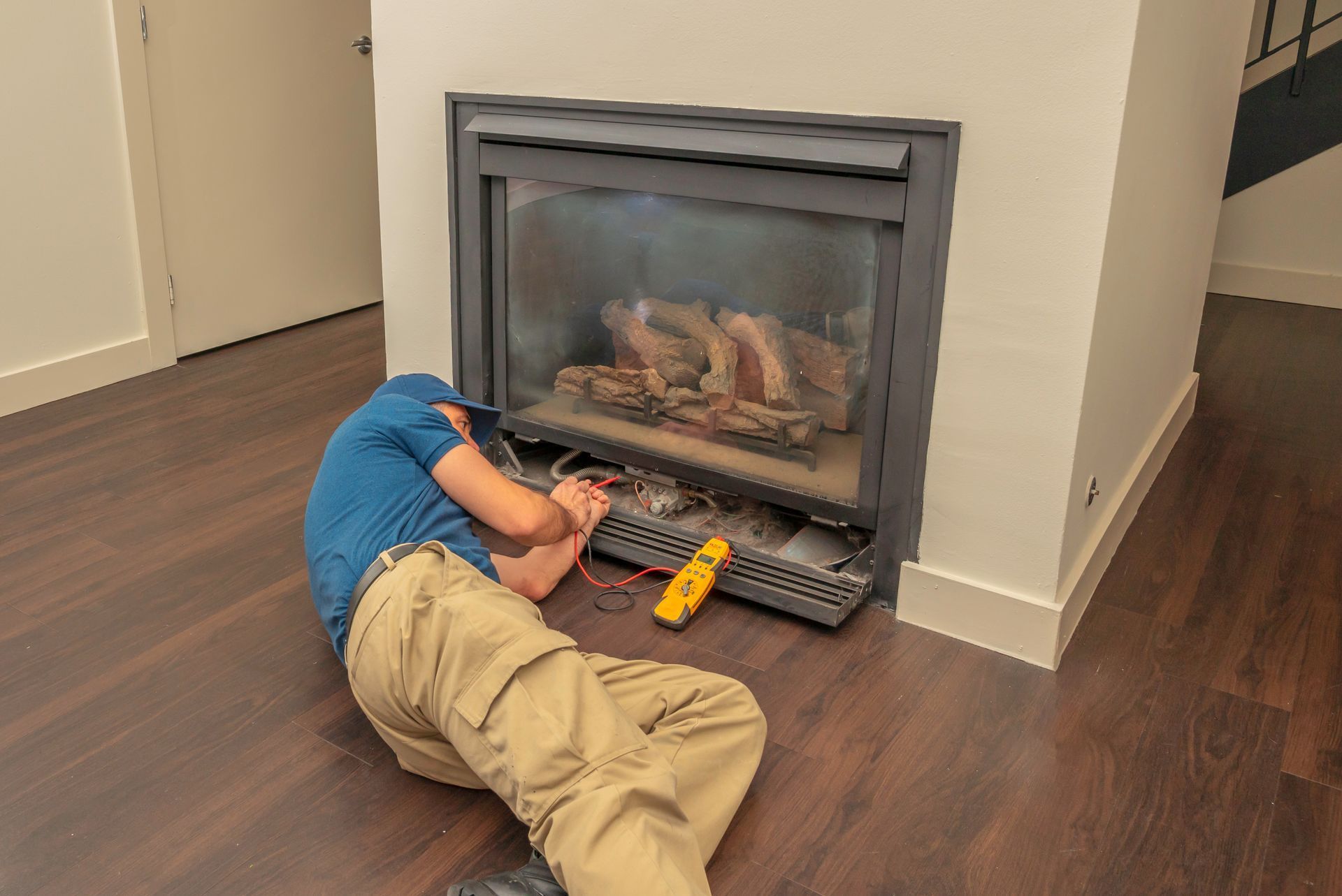 Person lying on the floor working inside a fireplace with tools nearby, in a room with hardwood floors.