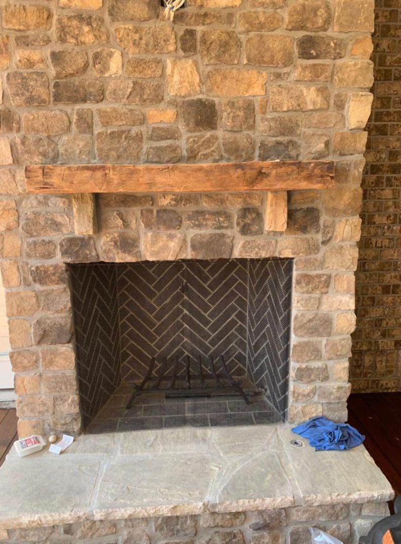 Stone fireplace with a wooden mantel and black herringbone firebox, with a gray hearth