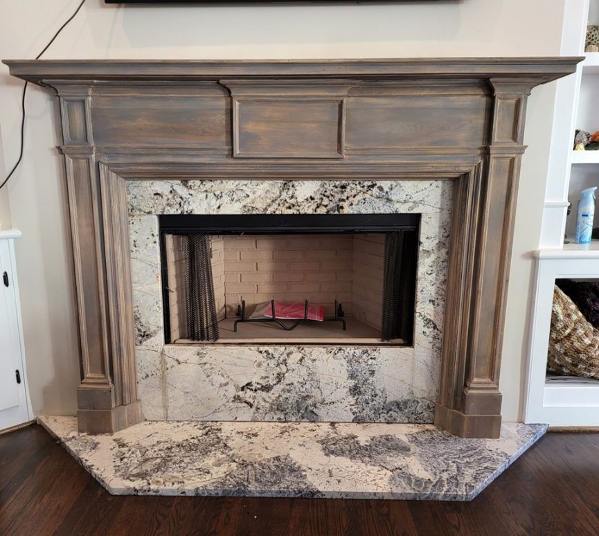Wooden fireplace mantel with gray stone surround and hearth in a living room.