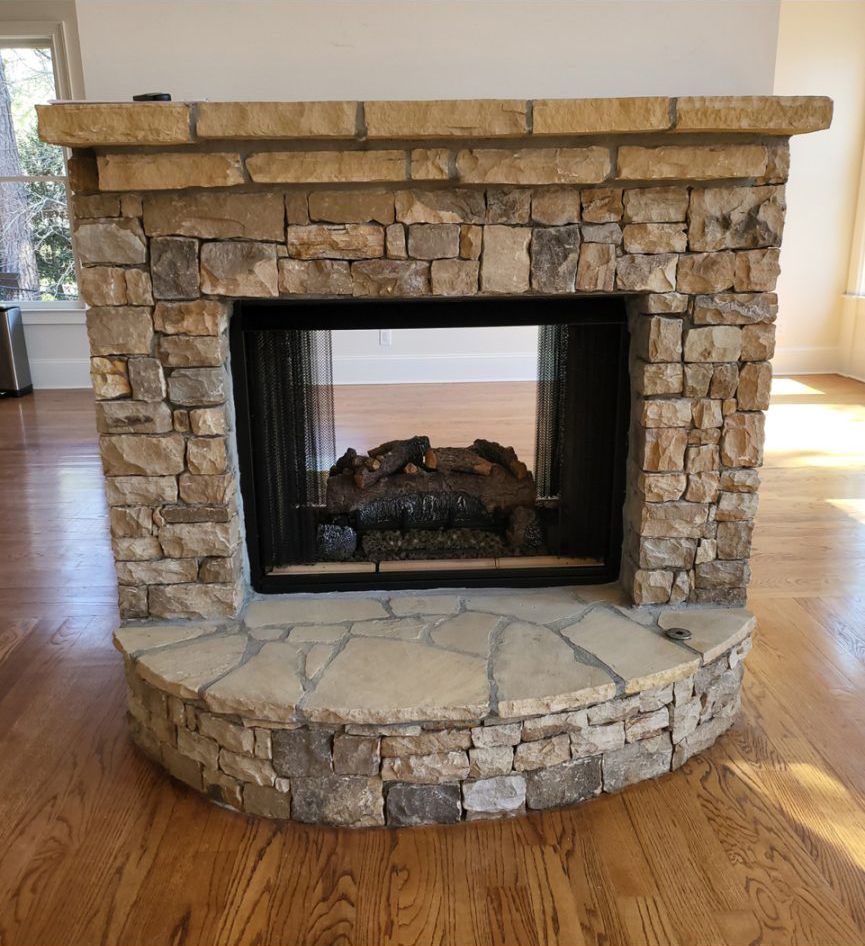 Stone fireplace with a black firebox and curved stone hearth in a hardwood-floored room