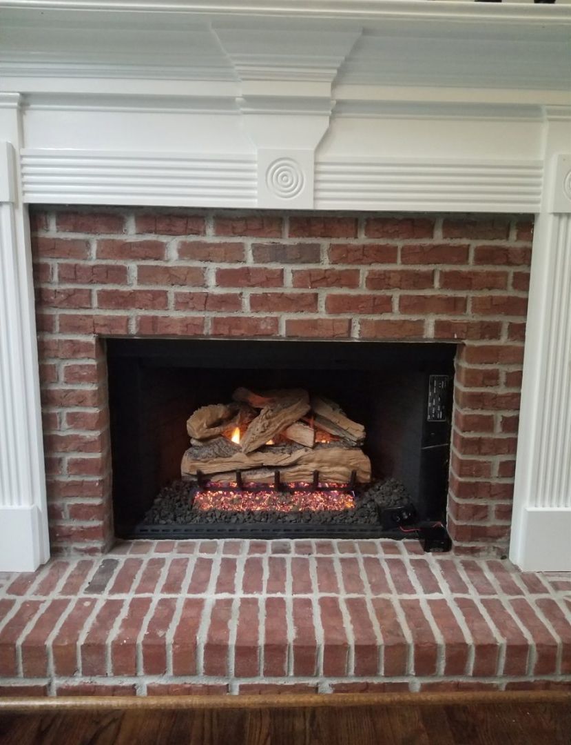 Brick fireplace with white mantel, red brick hearth, and stacked logs inside the firebox
