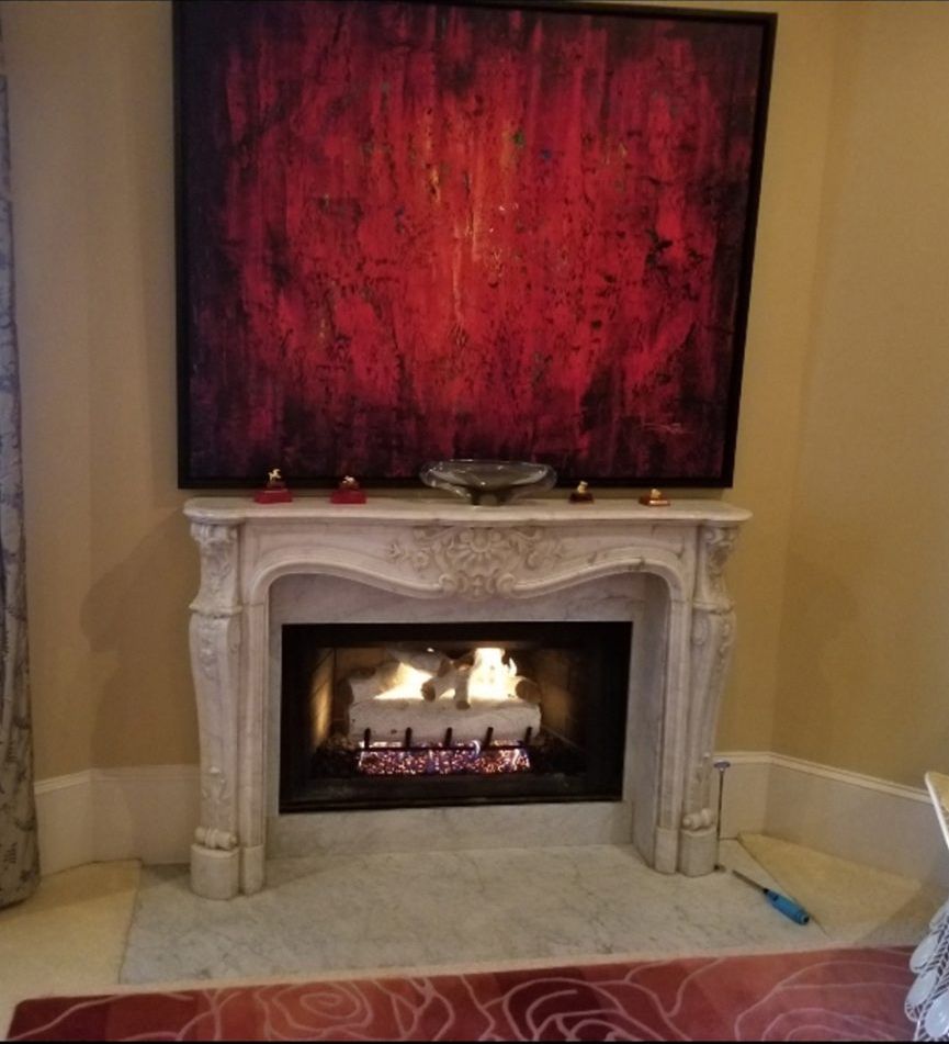 Living room fireplace with a glowing fire beneath a large red abstract painting
