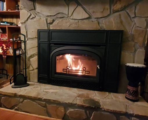 Lit black fireplace set in a stone hearth, with flames glowing in a cozy room.