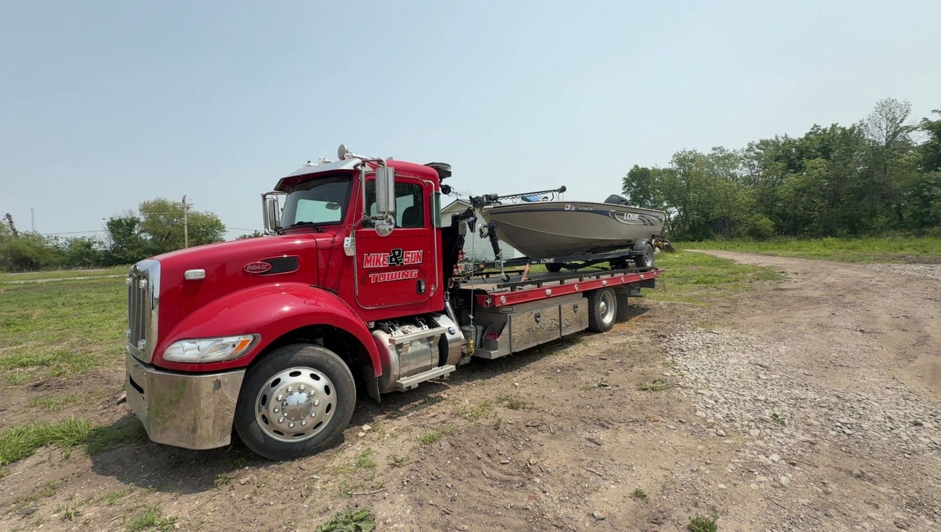 Red cement truck on a dirt road, parked on grassy land under a blue sky.