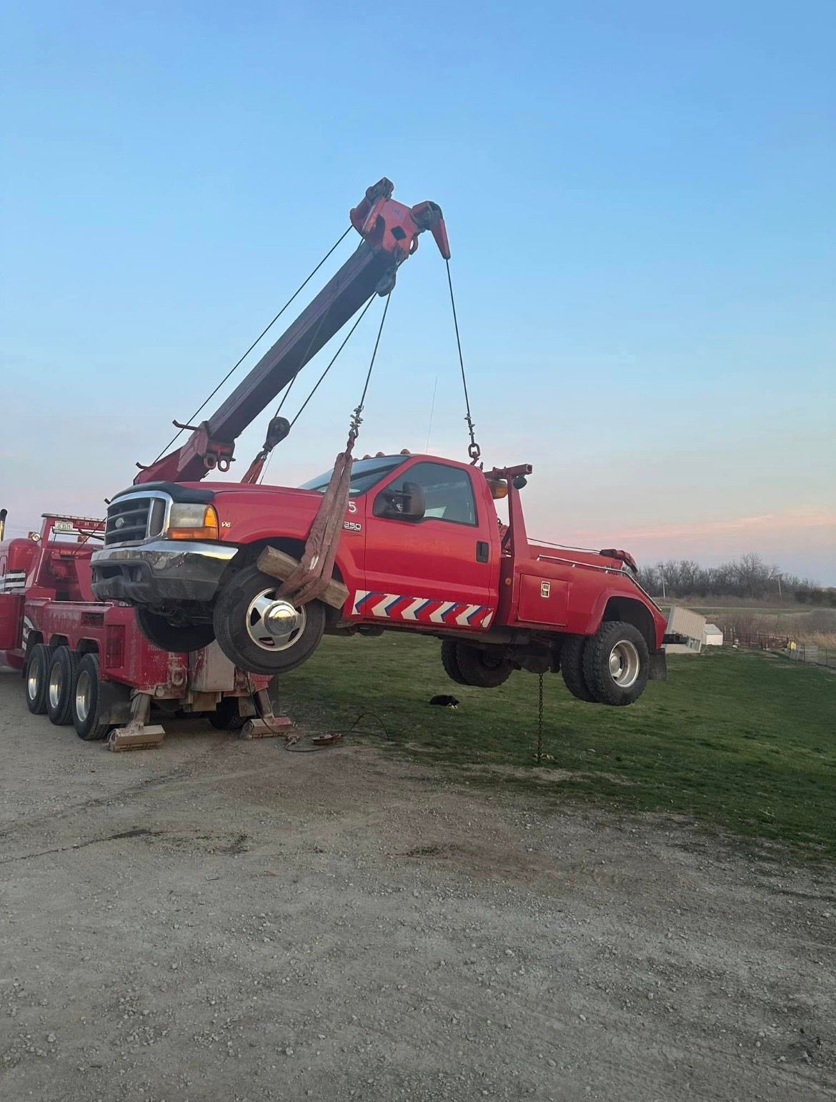 Red tow truck lifting another red tow truck in a field.