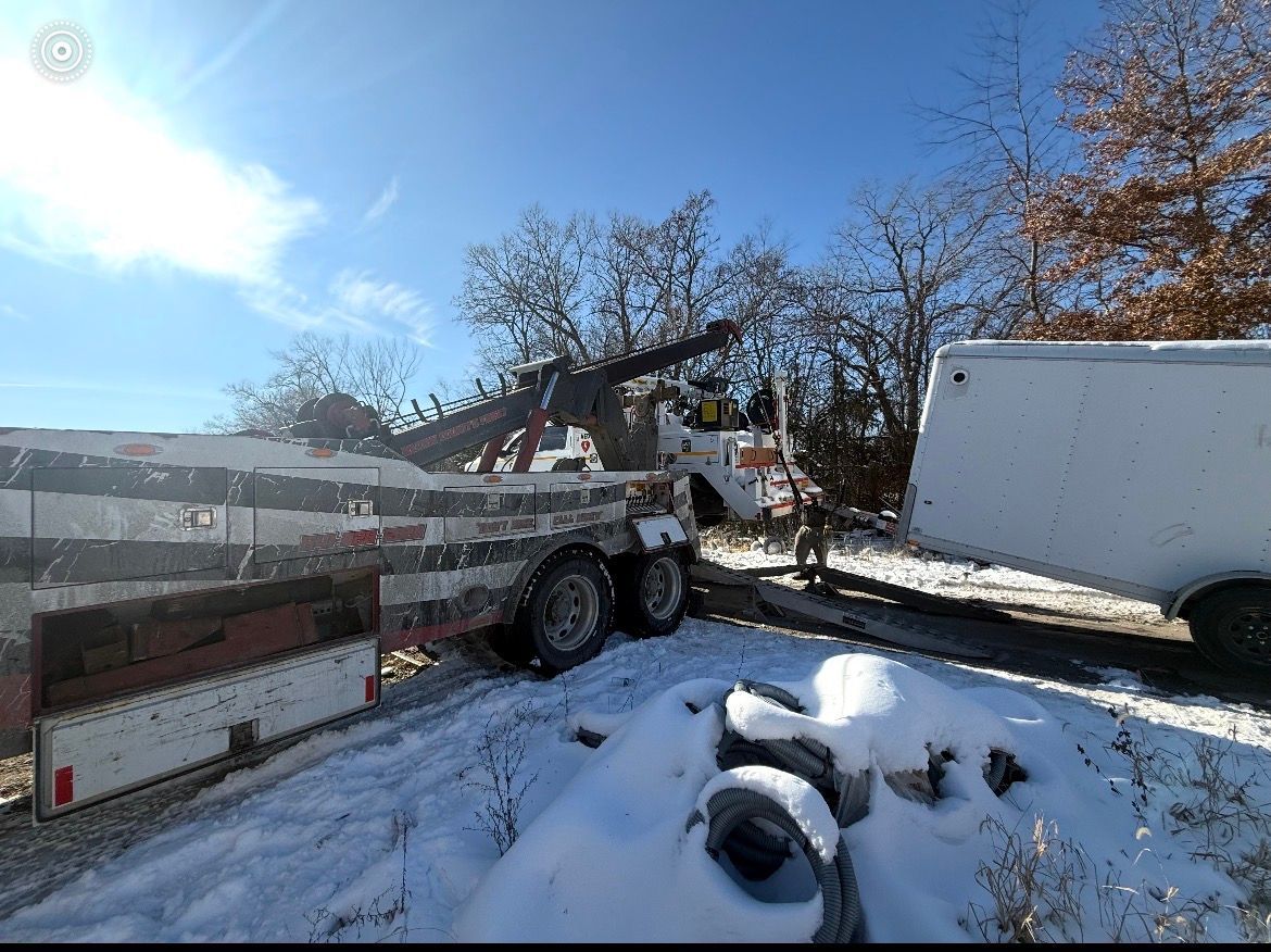 Tow truck loading a vehicle onto a flatbed on a snow-covered roadside, sunny day.