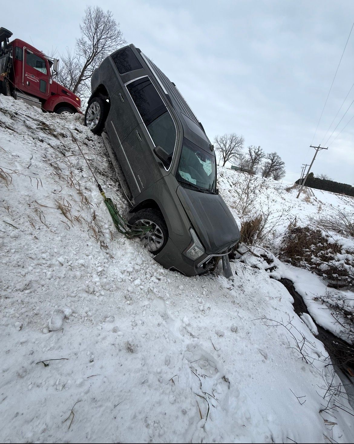 SUV stuck in snow on the side of a snowy embankment, near a red tow truck.