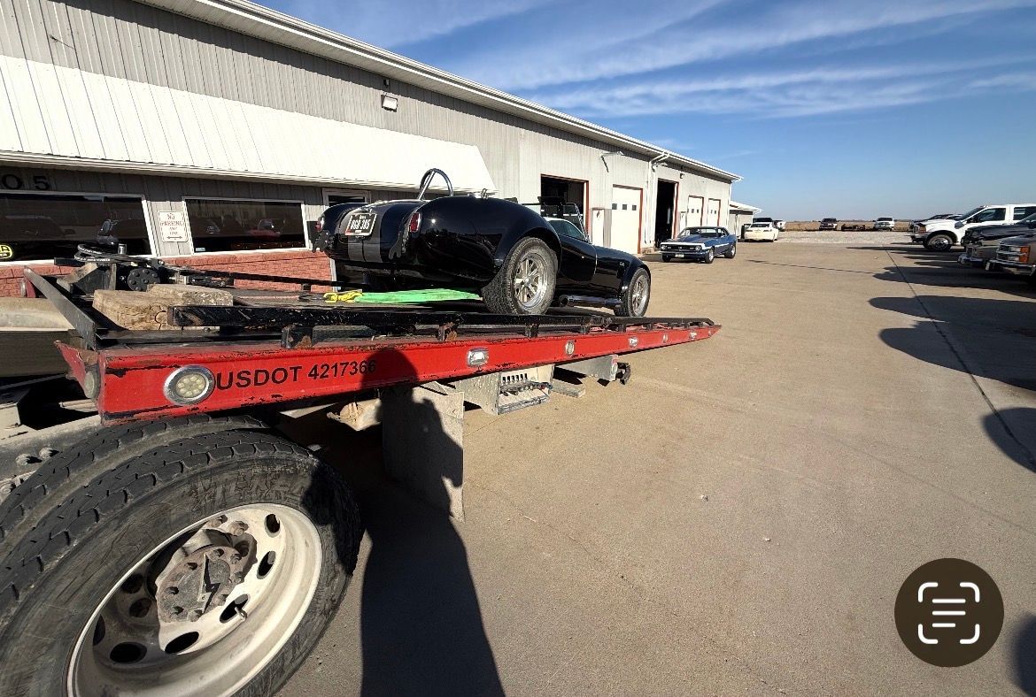 Black sports car on a red tow truck, parked in front of a building on a sunny day.