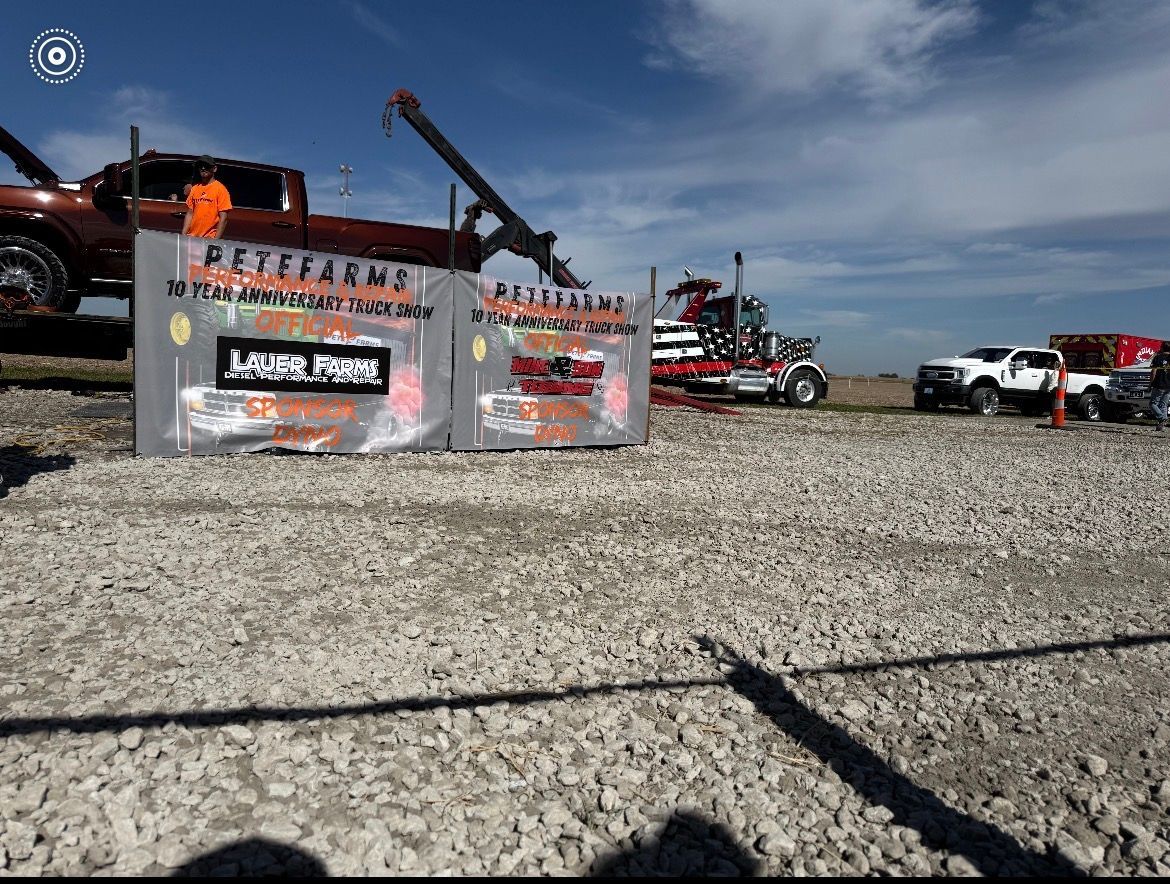 A truck pull event with trucks and equipment staged on gravel under a blue sky.