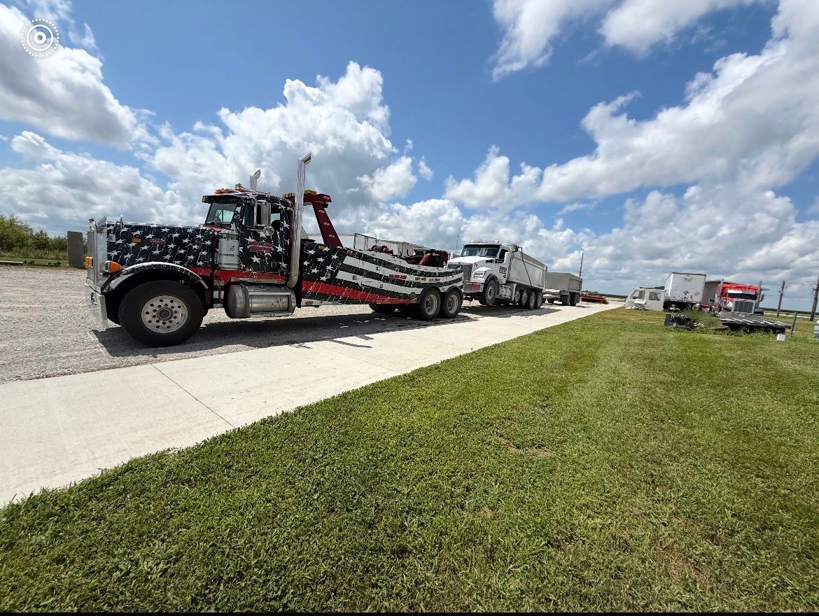 Tow truck hauling a white semi-truck on a sunny day. The tow truck has a colorful design.