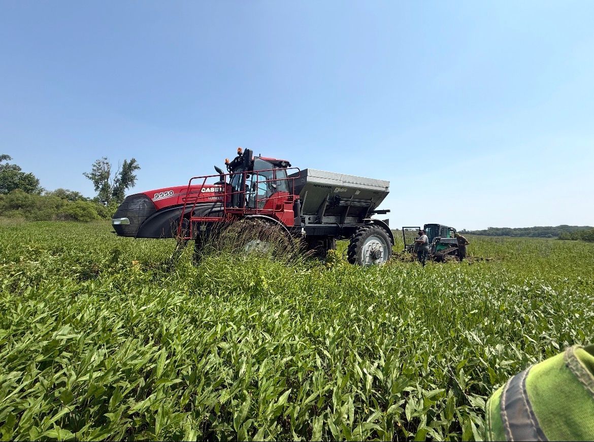 Red tractor applying fertilizer in a green field under a clear blue sky.