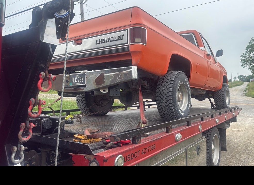 Orange Chevrolet pickup truck being towed on a flatbed tow truck.