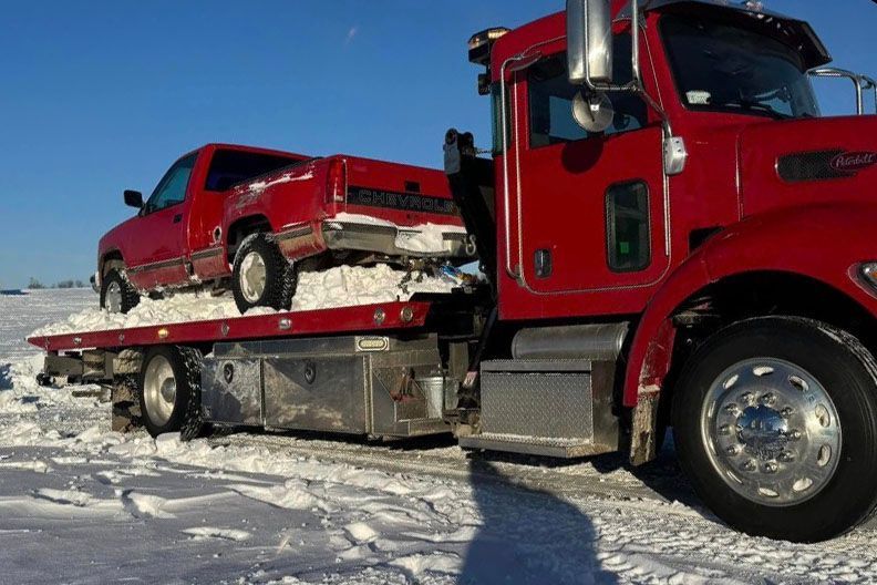 Red pickup truck being towed by a red tow truck on a snowy field.