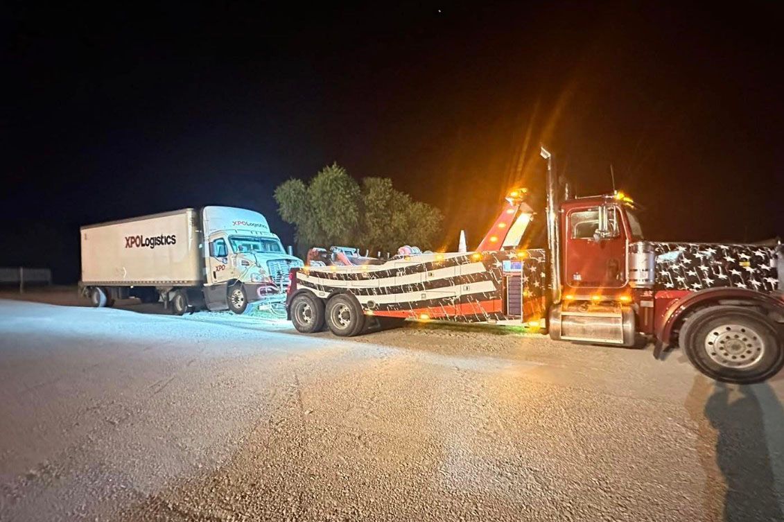 Tow truck pulling a box truck at night. Both vehicles have lights on.