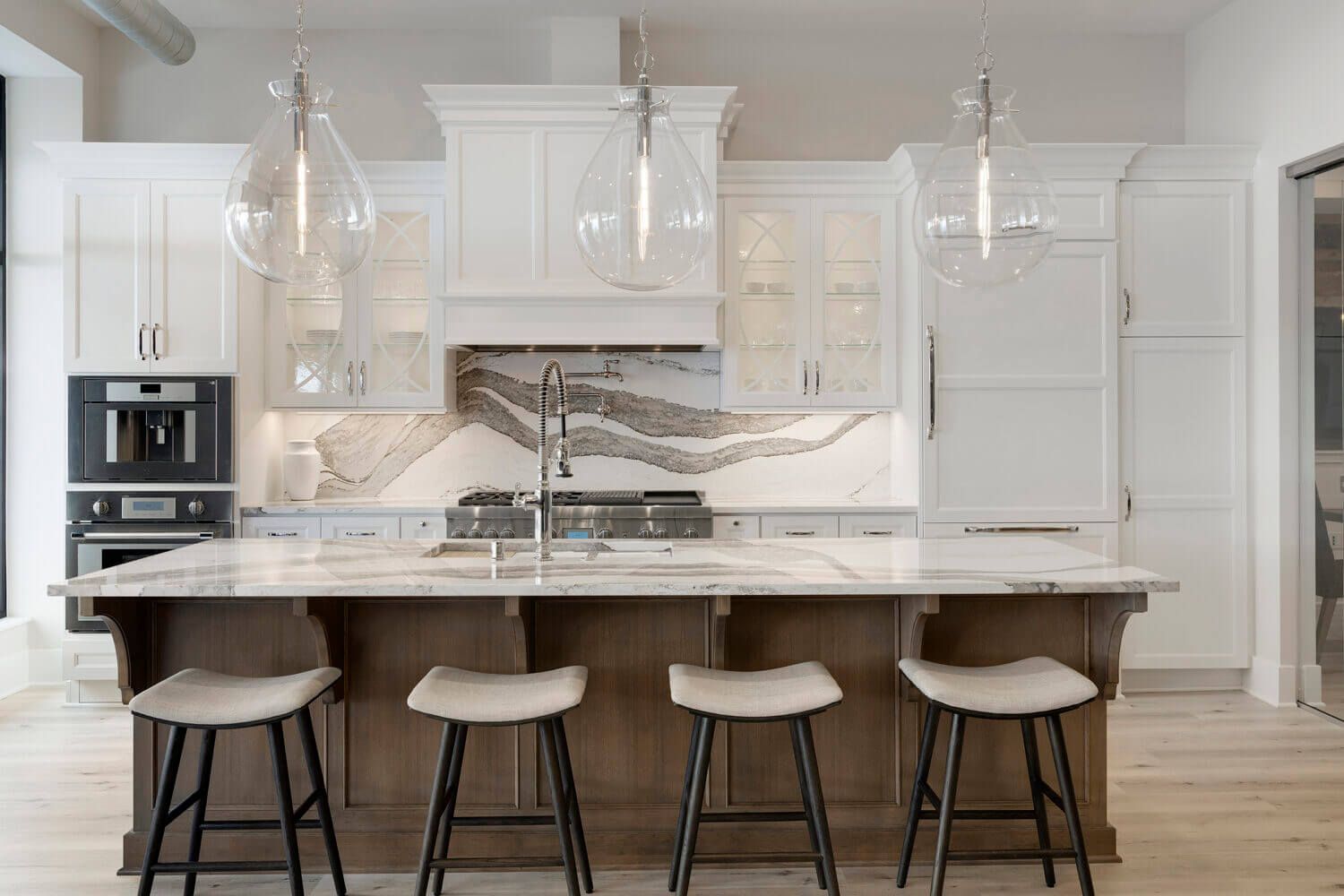 Modern kitchen with white cabinets, marble backsplash, wooden island, and pendant lights.