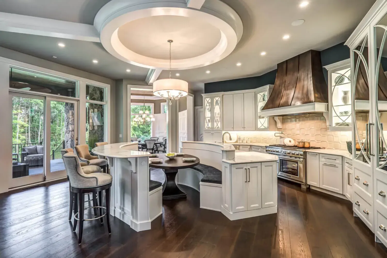 Elegant, light-filled kitchen with a curved island, dark wood floor, and large range hood.