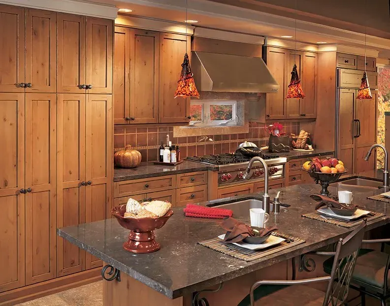 Kitchen with light-colored wooden cabinets, island with countertop, and hanging pendant lights.
