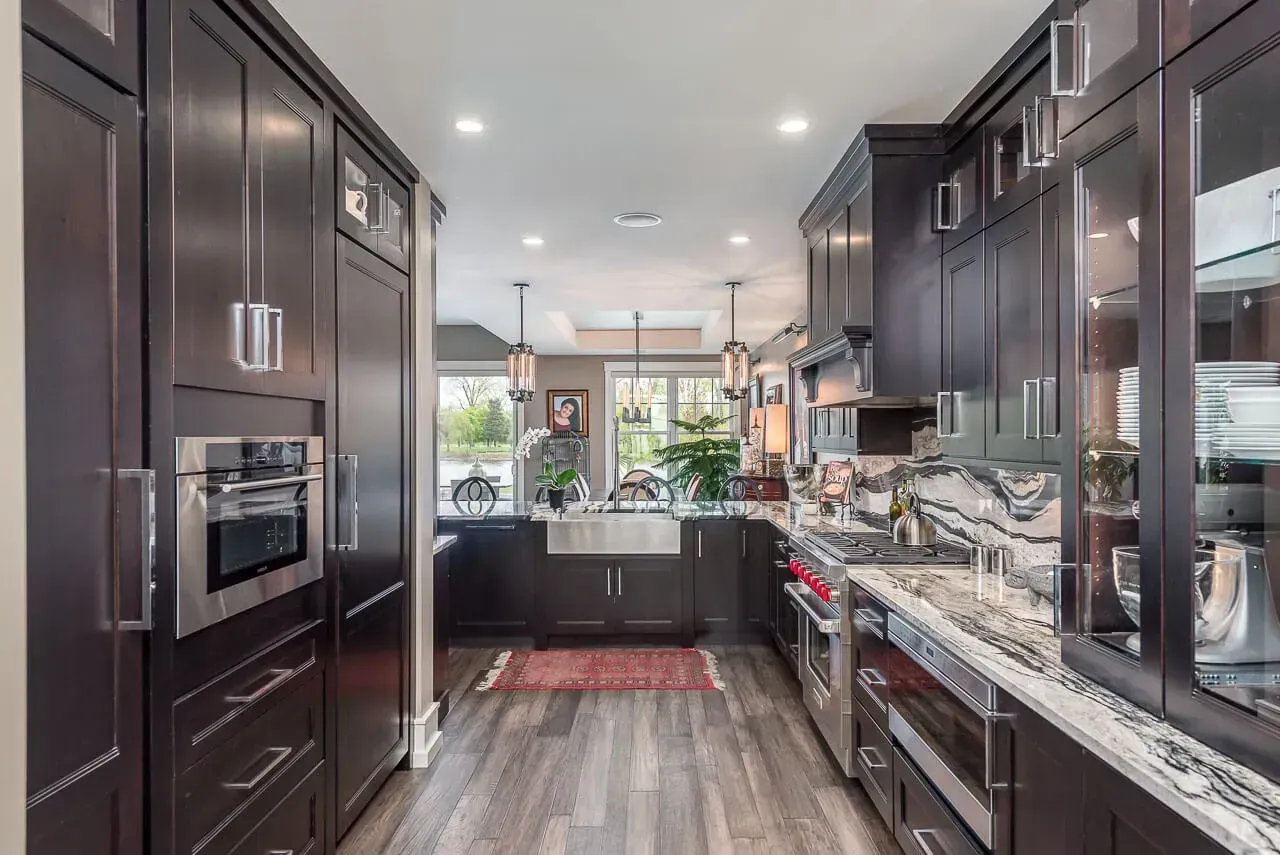 Dark wood kitchen with stainless steel appliances, granite countertops, and a view through the open doorway.