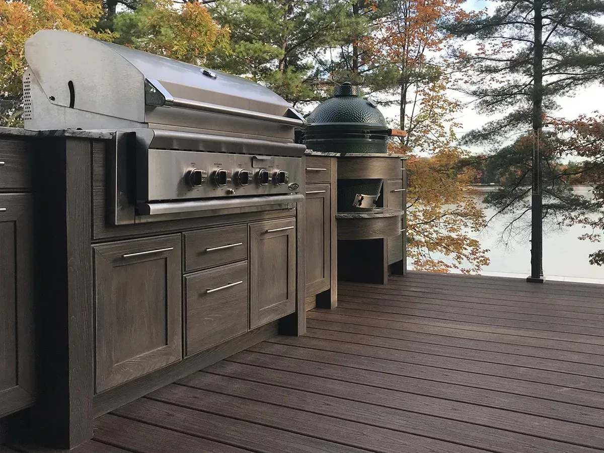 Outdoor kitchen with grill and Big Green Egg overlooking a lake with fall foliage.