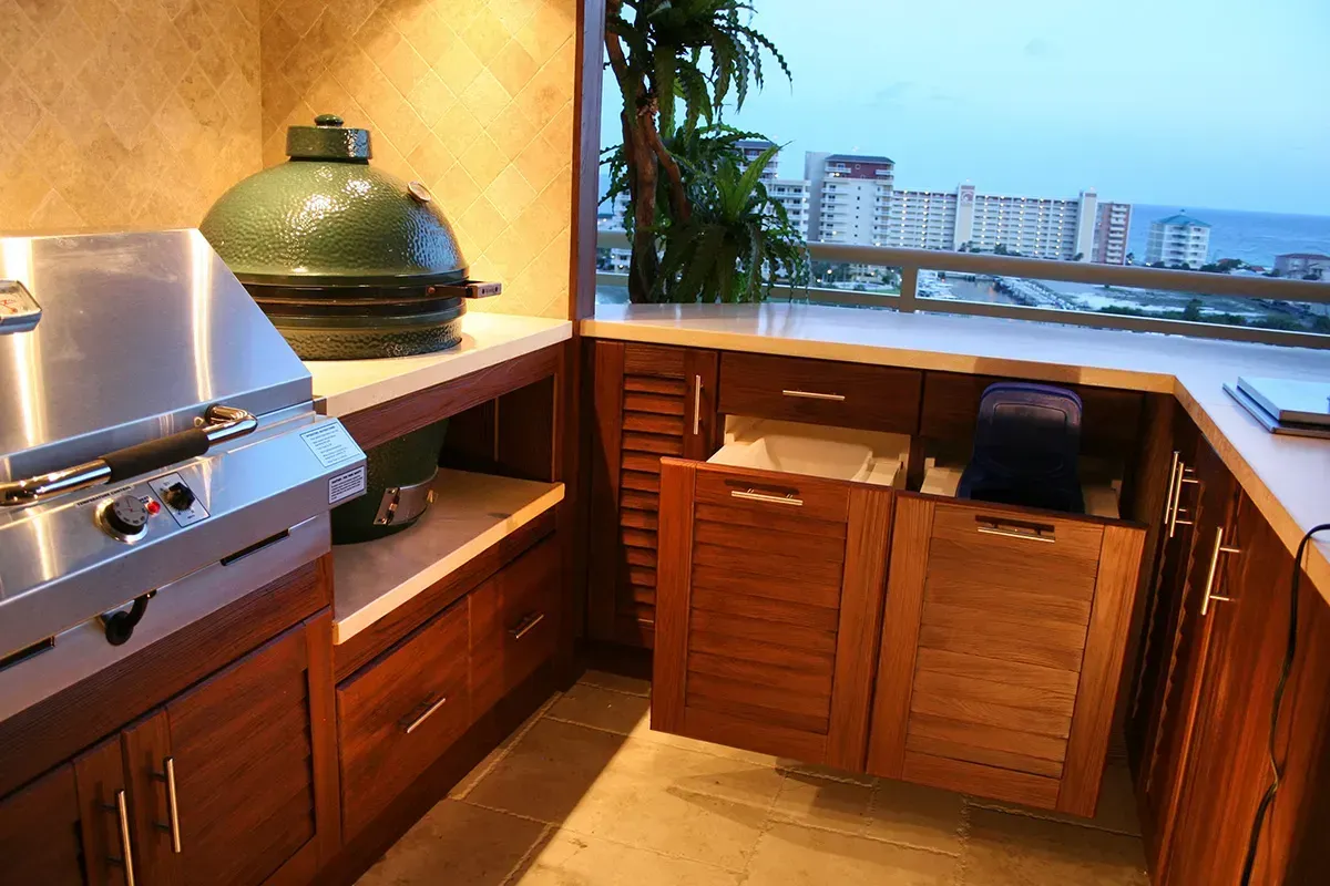 Outdoor kitchen with stainless steel grill, Big Green Egg, and wooden cabinets overlooking a city skyline.