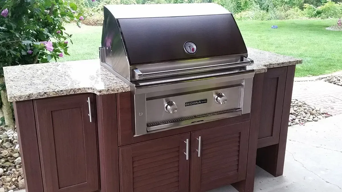 Outdoor grill set on a brown cabinet with granite countertop, set on a patio.