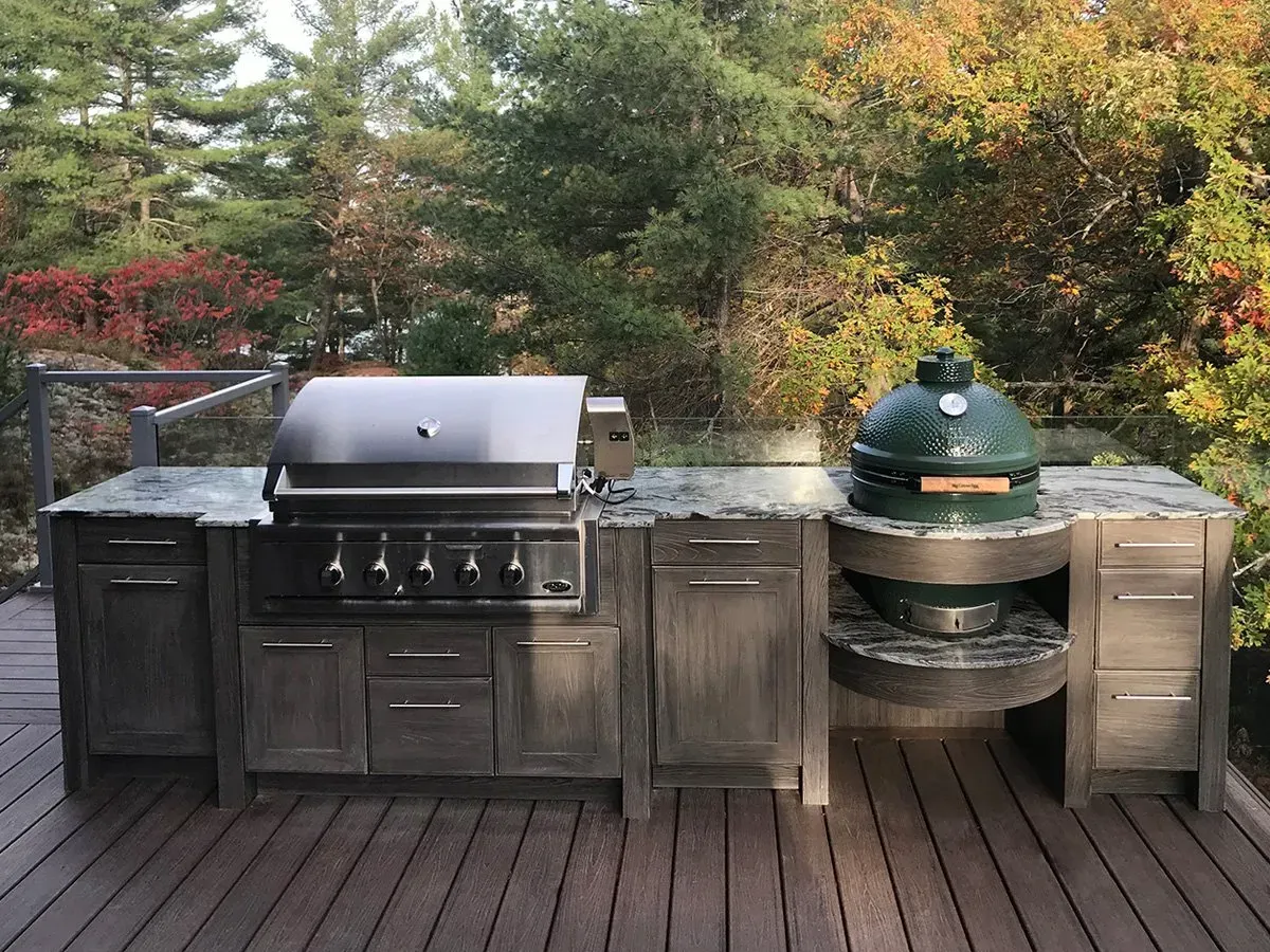 Outdoor kitchen with grill and Big Green Egg on a wooden deck surrounded by trees.