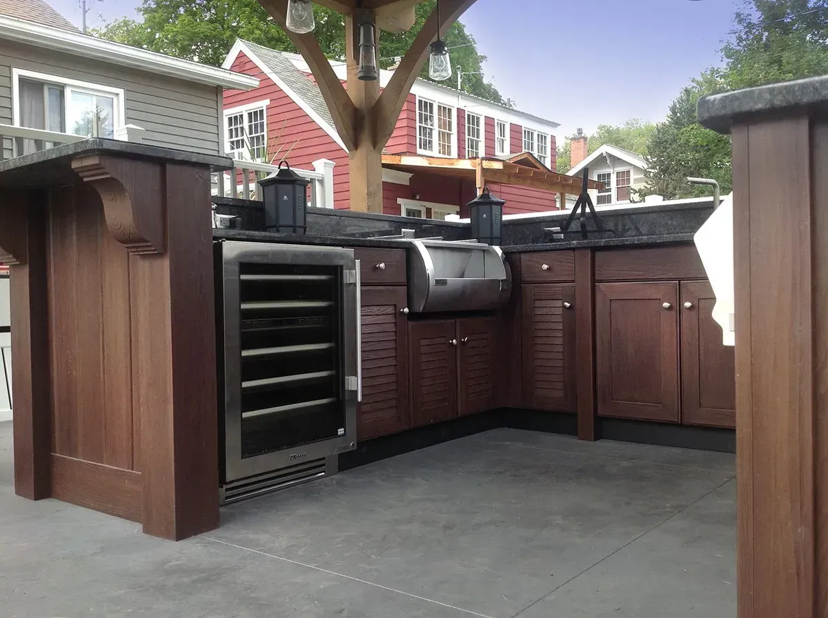 Outdoor kitchen with a stainless steel grill and a wine cooler, surrounded by wooden cabinets.