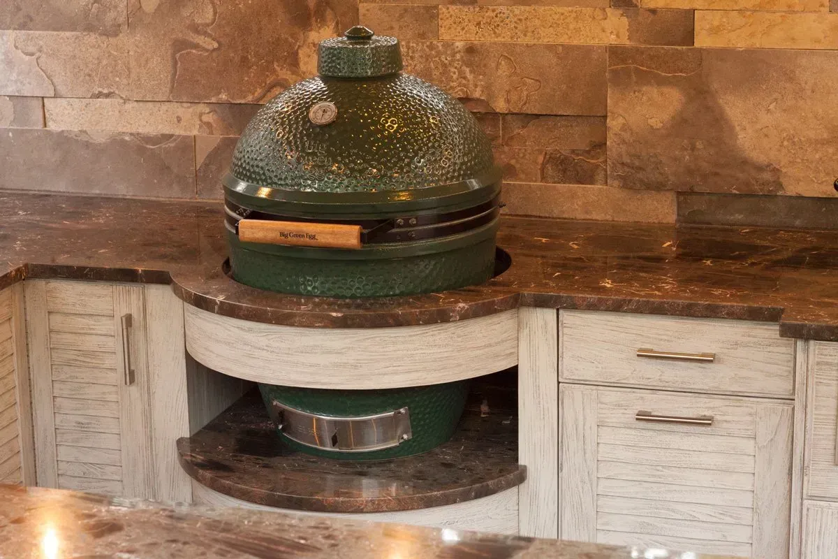 Green egg-shaped grill built into a stone-covered countertop with cabinets below.