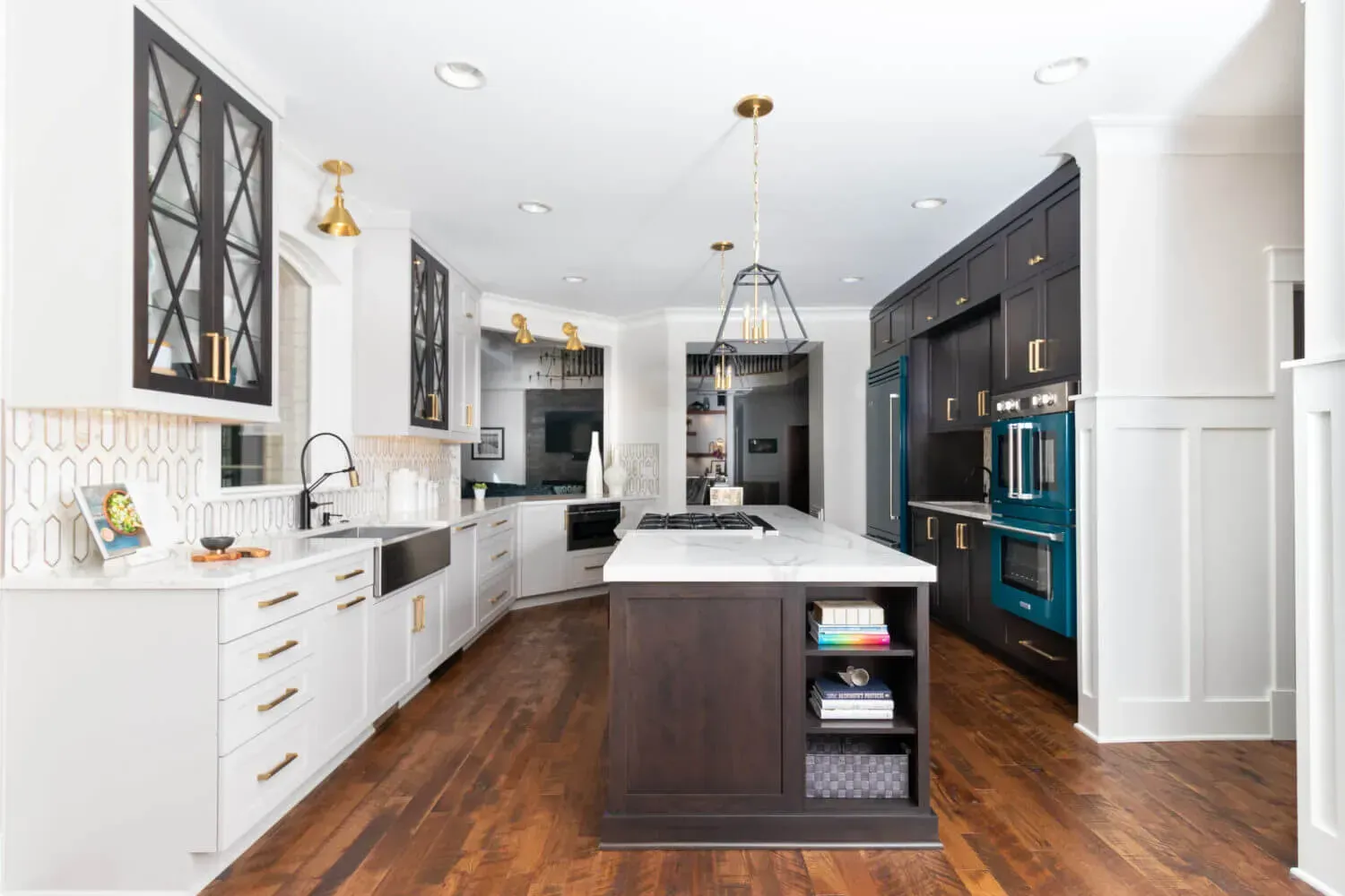Modern kitchen with white and dark cabinets, island with stovetop, wood floors, and teal oven.