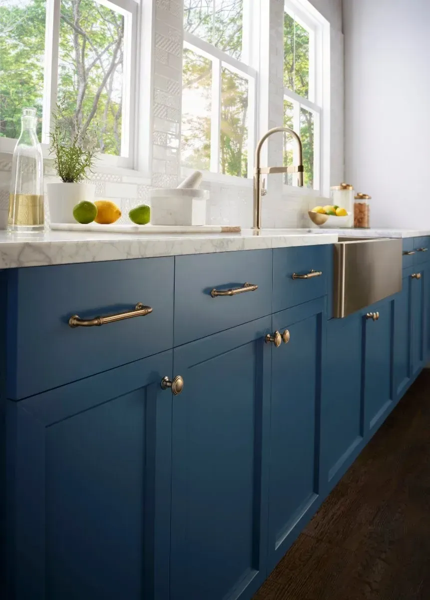 Blue kitchen cabinets with gold hardware, stainless steel sink, and a sunny window.