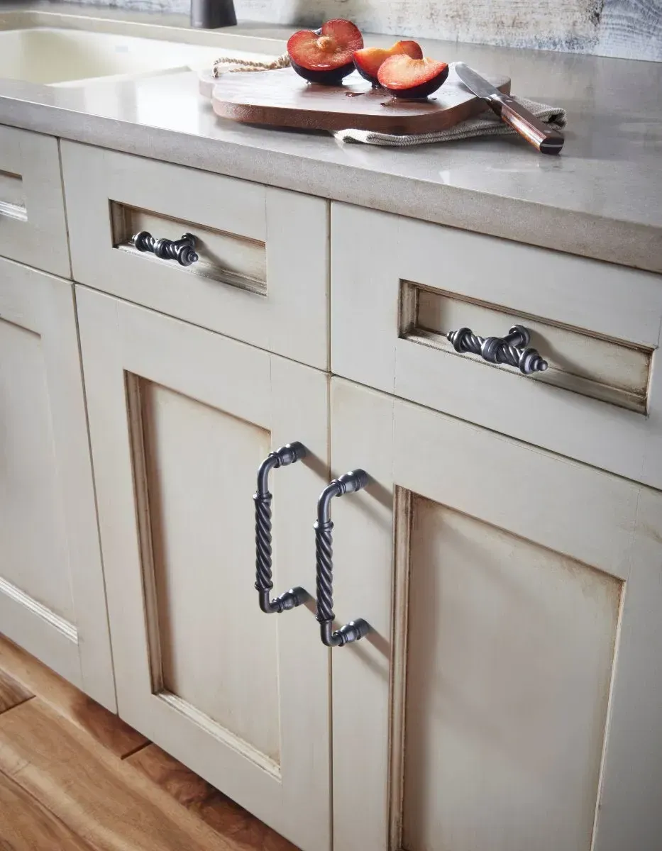Cream-colored kitchen cabinets with decorative metal hardware. A cutting board with fruit and a knife rests on the counter.
