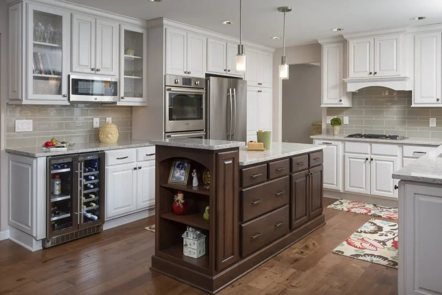 White and brown kitchen with island, stainless steel appliances, and hardwood floors.