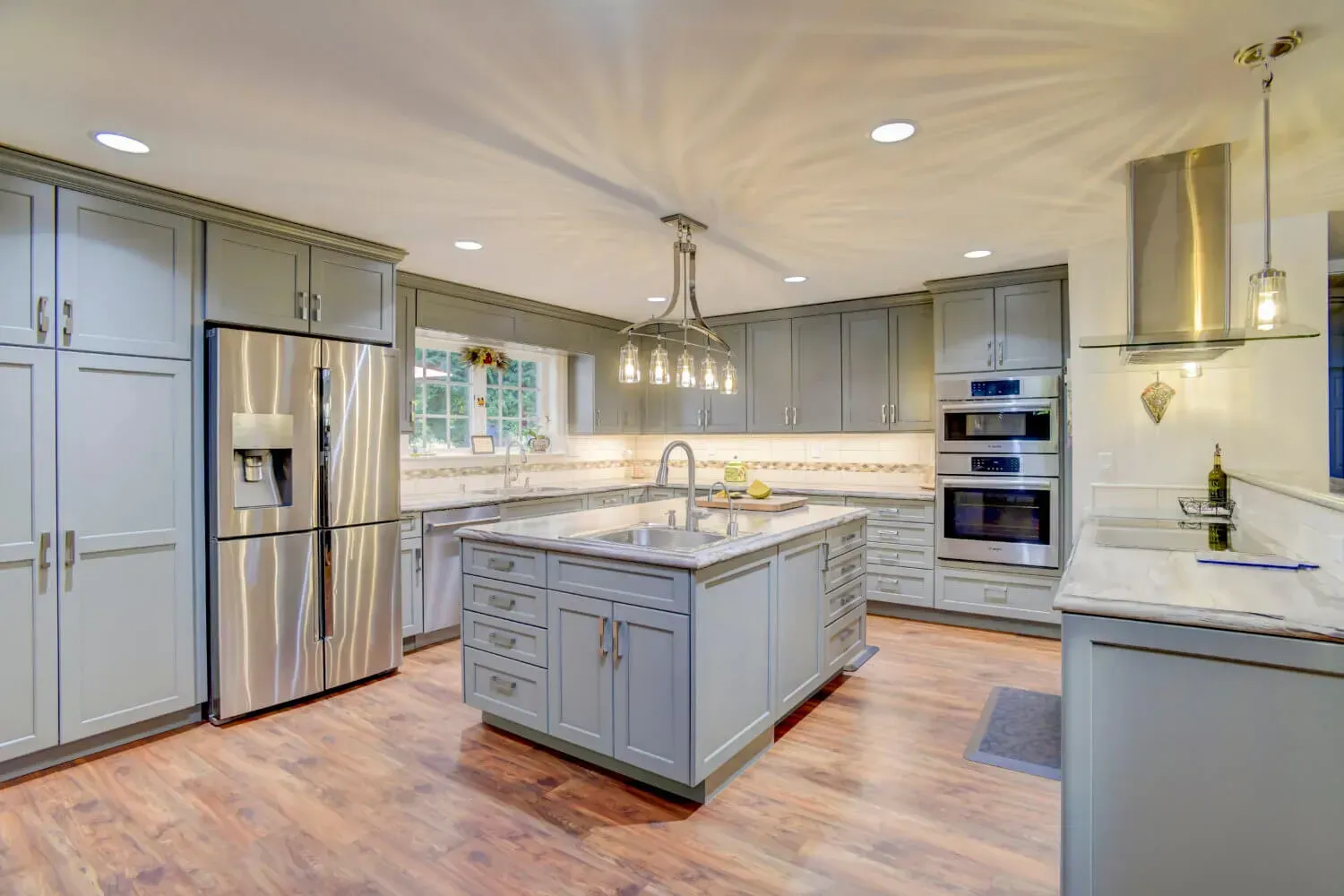 Modern kitchen with gray cabinets, stainless steel appliances, and wooden floor.