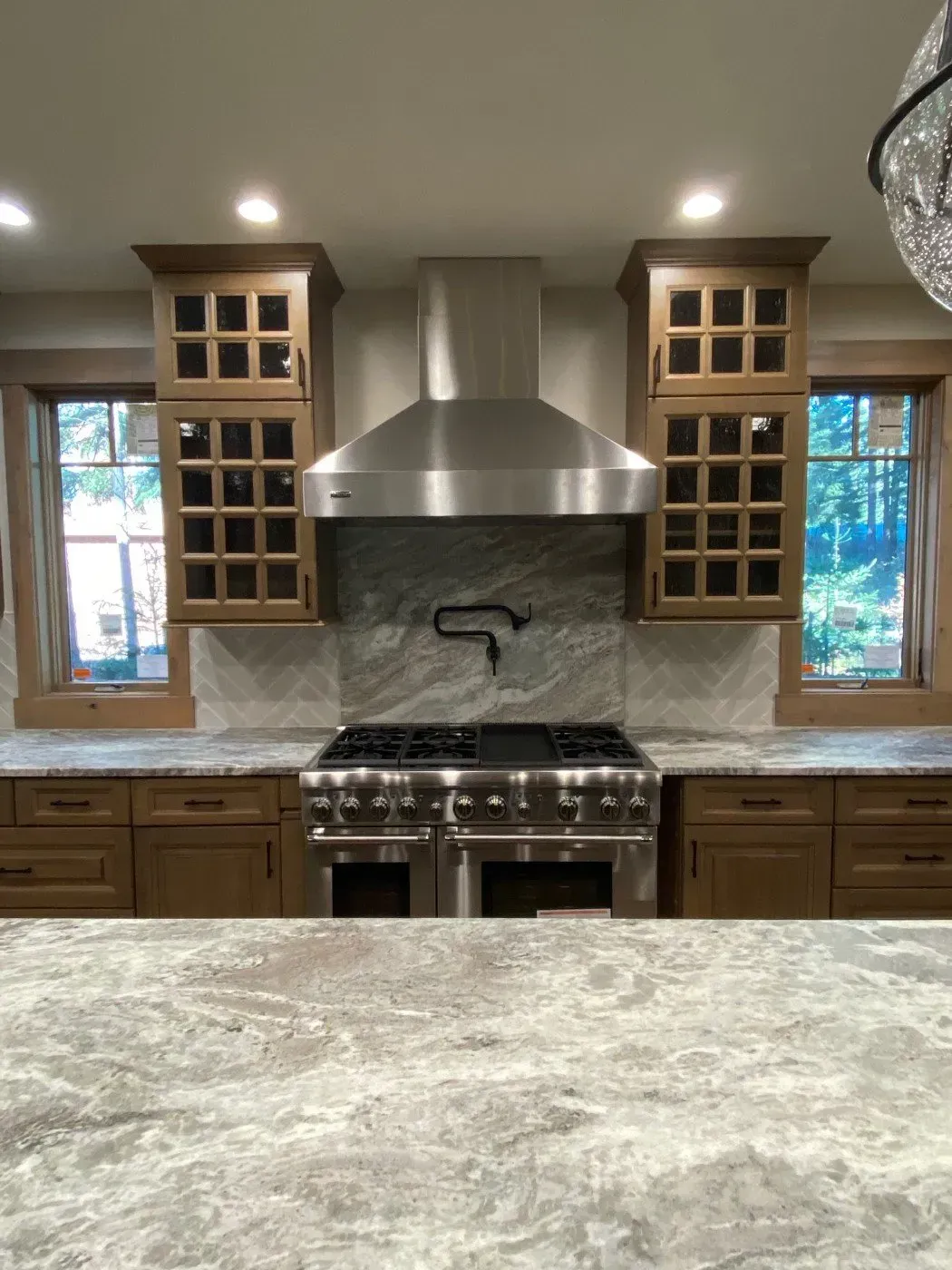 Kitchen with stainless steel range hood, stove, cabinets, windows, and light countertop.