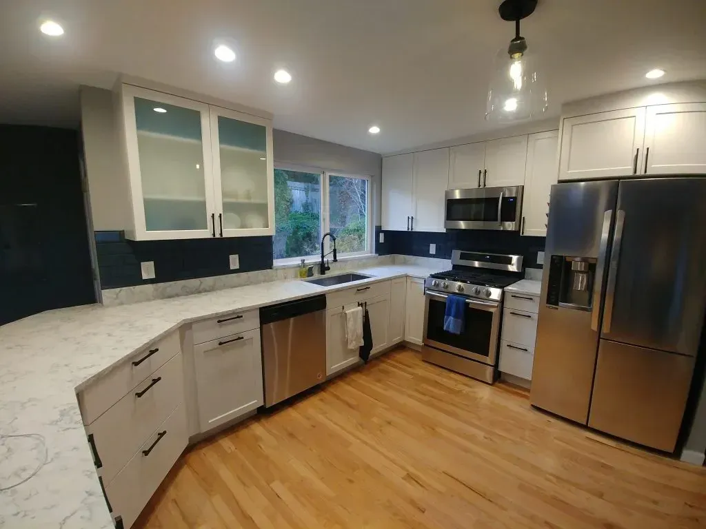 Modern kitchen with white cabinets, stainless steel appliances, and wood floors.