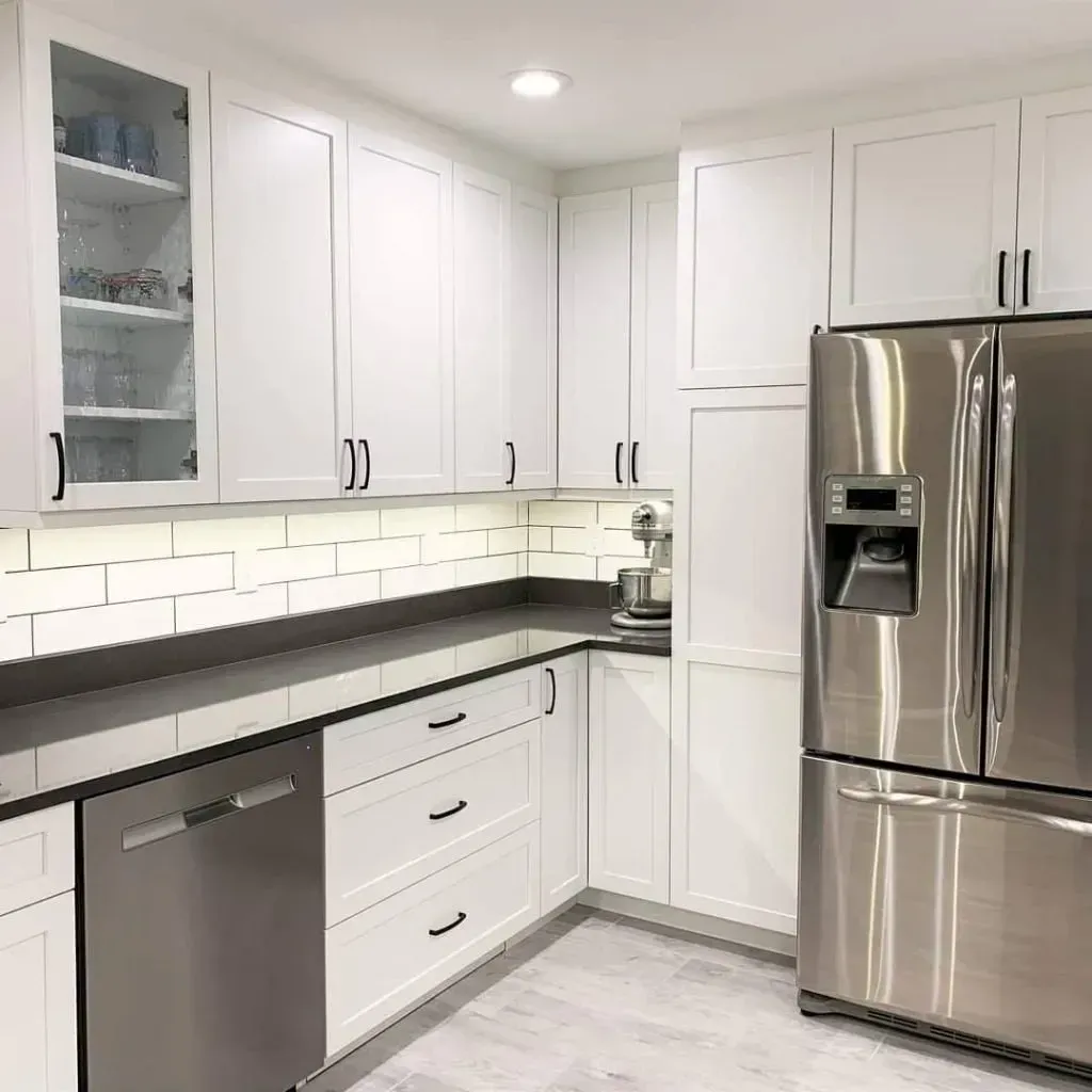 White kitchen with stainless steel appliances, dark countertops, and tile backsplash.
