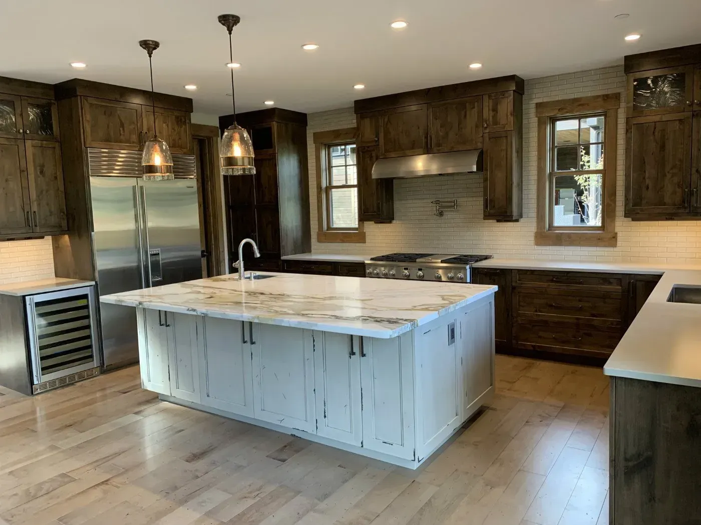 Kitchen with wood cabinets, white island, stainless steel appliances, and wood floors.