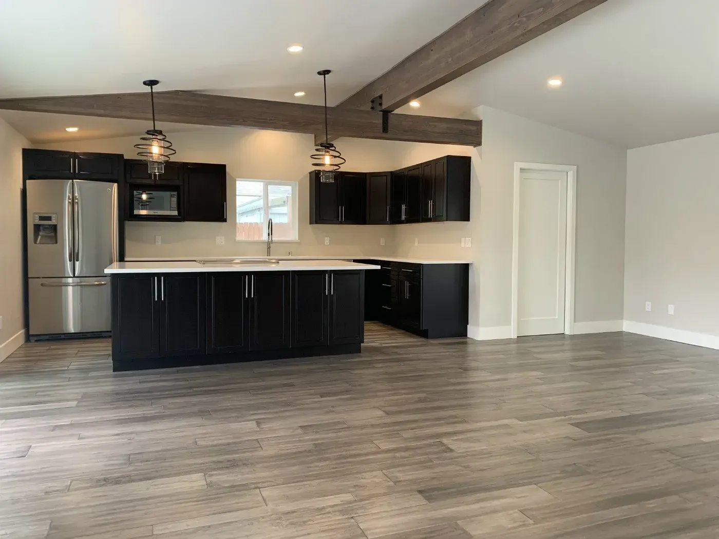 Modern kitchen with black cabinets, stainless steel appliances, island, and wood-look flooring.