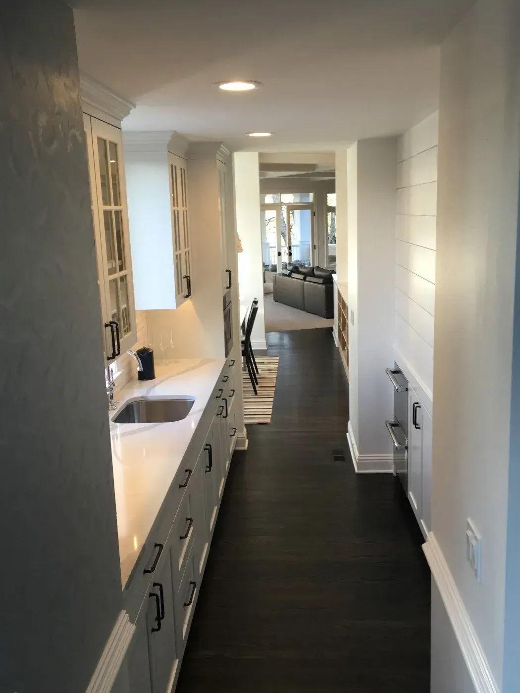 Narrow hallway with a white countertop and dark wood floor leading to a living area.