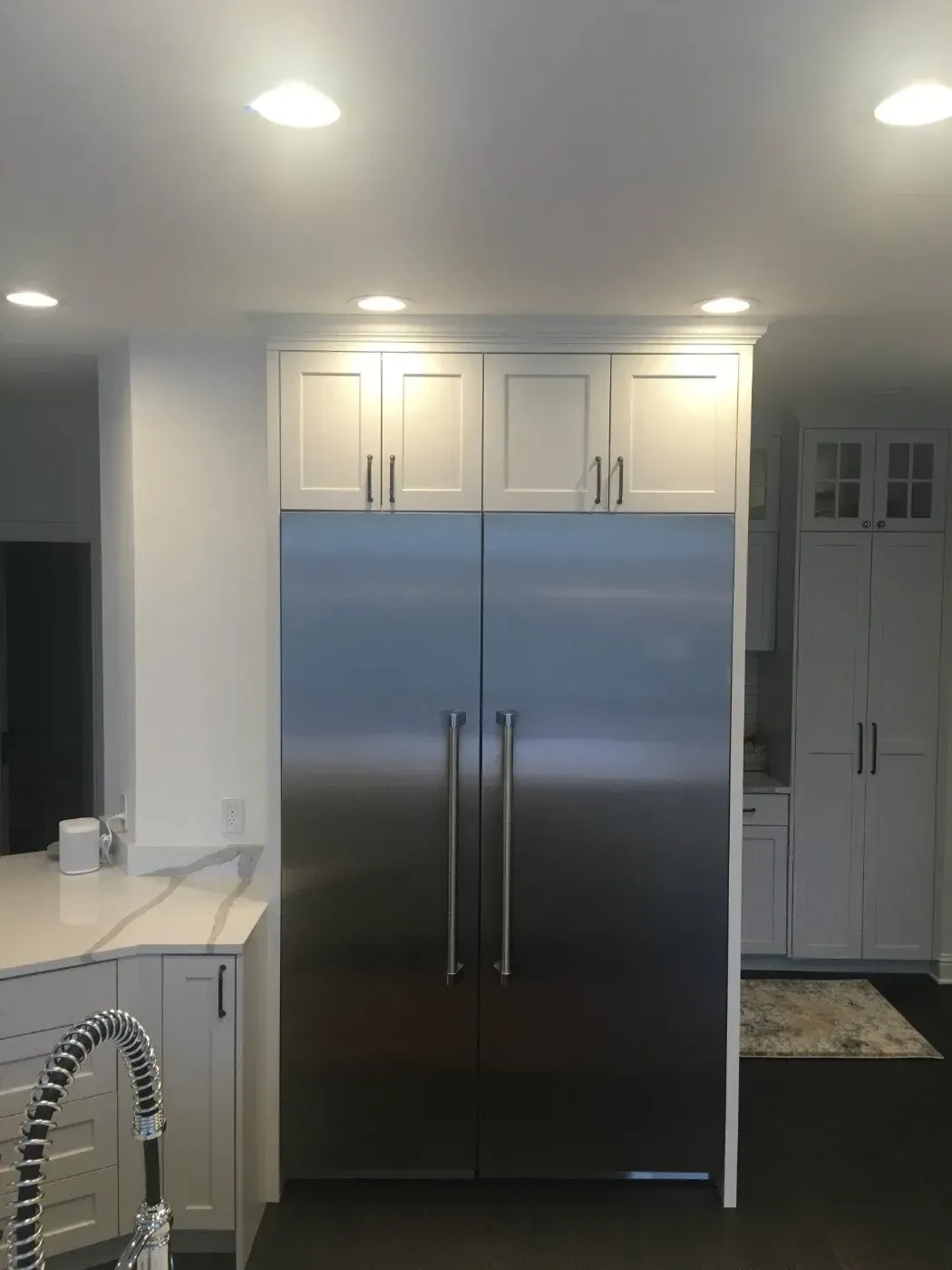 Stainless steel refrigerator with white cabinetry in a kitchen setting.