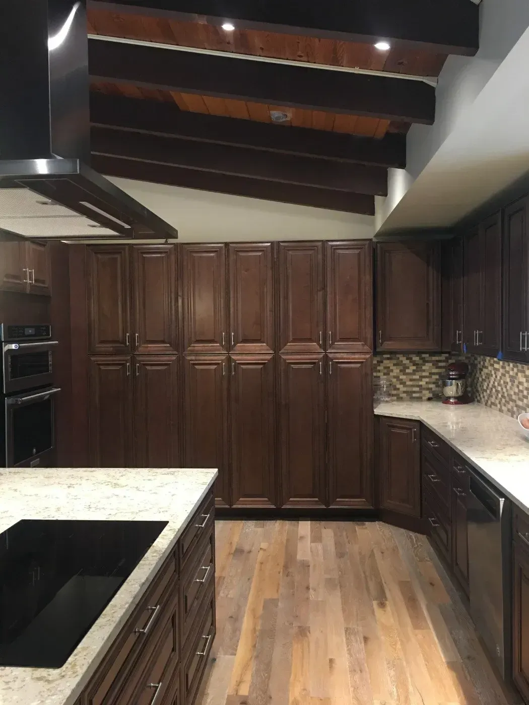 Kitchen with dark wood cabinets, light countertops, wooden beams, and hardwood floor.