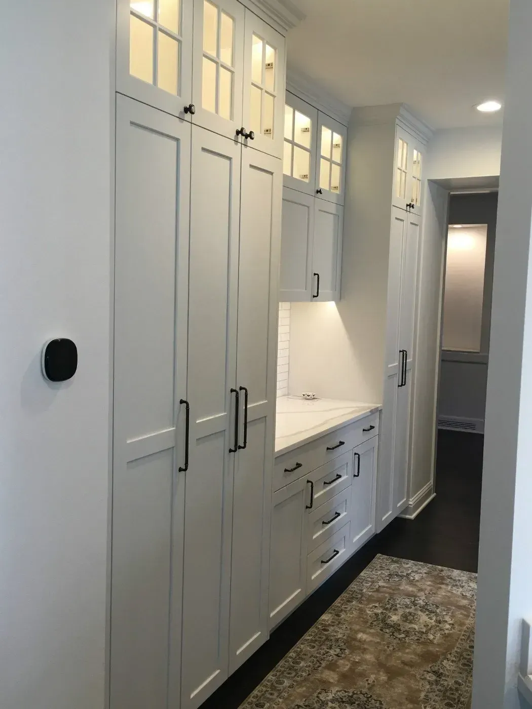 White built-in cabinets with black hardware and a small countertop, in a hallway with a patterned rug.