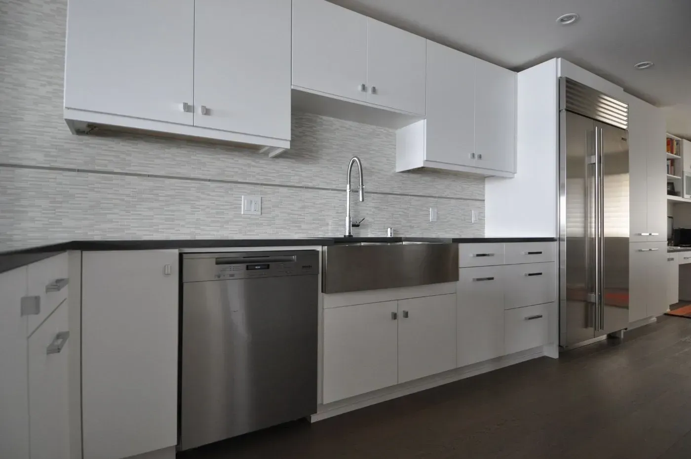 Modern white kitchen with stainless steel appliances, dark countertops, and tile backsplash.